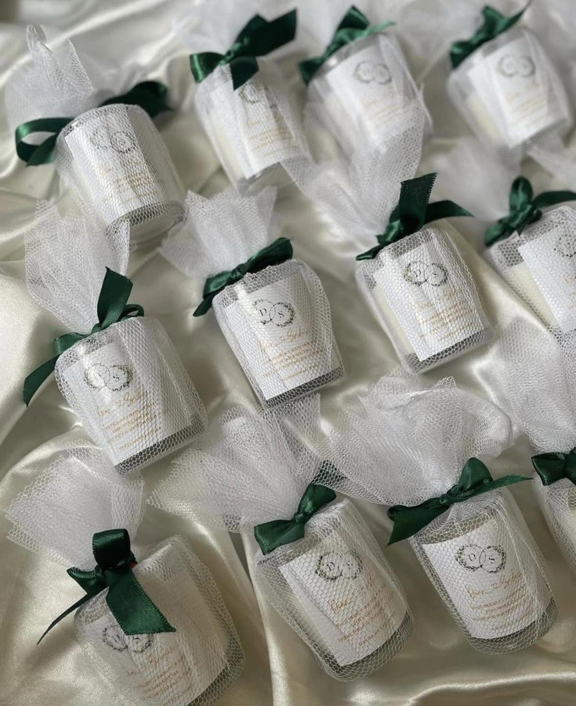 Mini white candles in glass jars wrapped in white tulle with green ribbons.