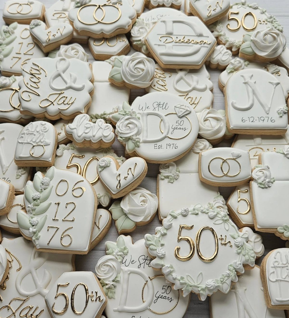 White iced anniversary cookies with gold lettering and frosting roses in various shapes.