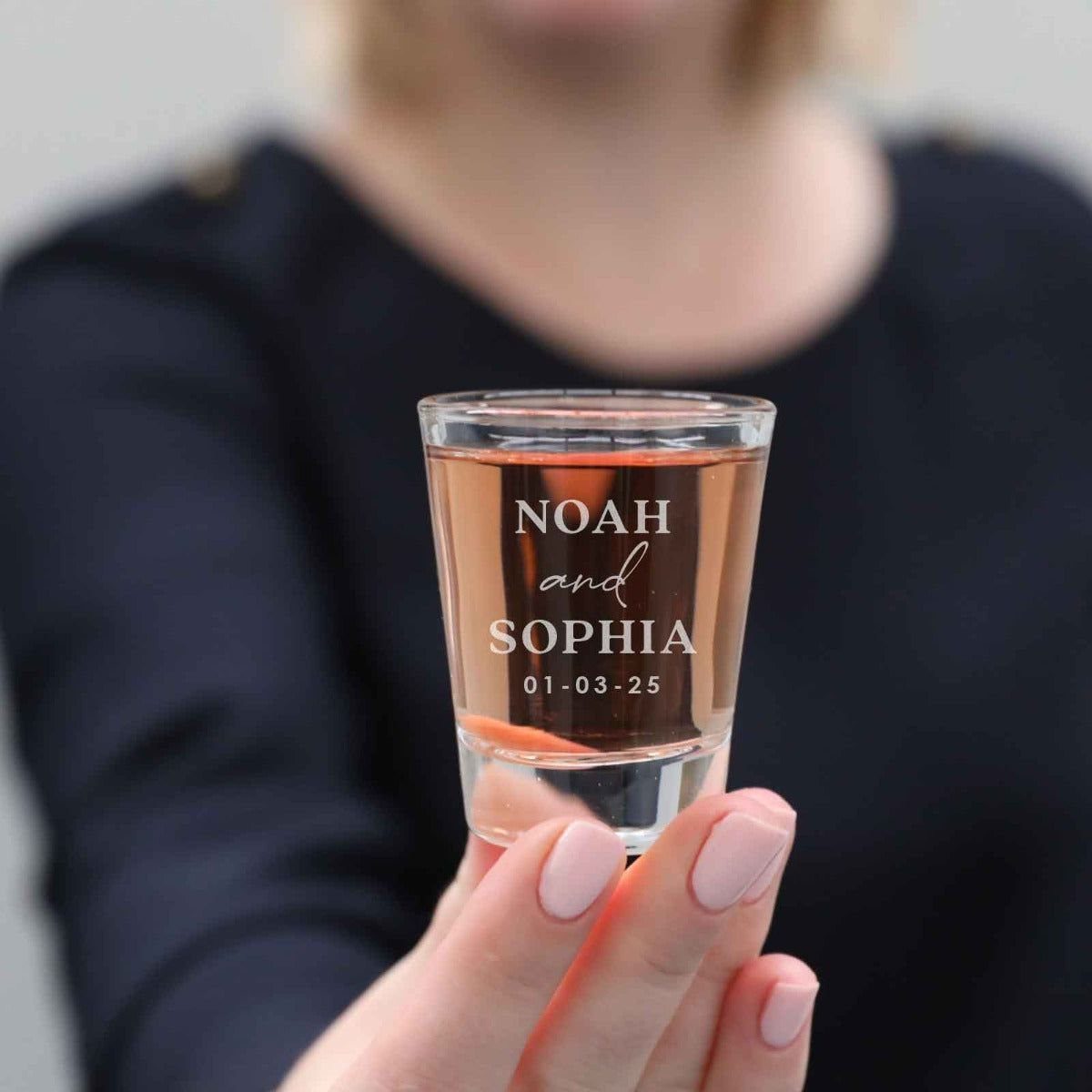 Engraved shot glass with names and date held by a person's hand.