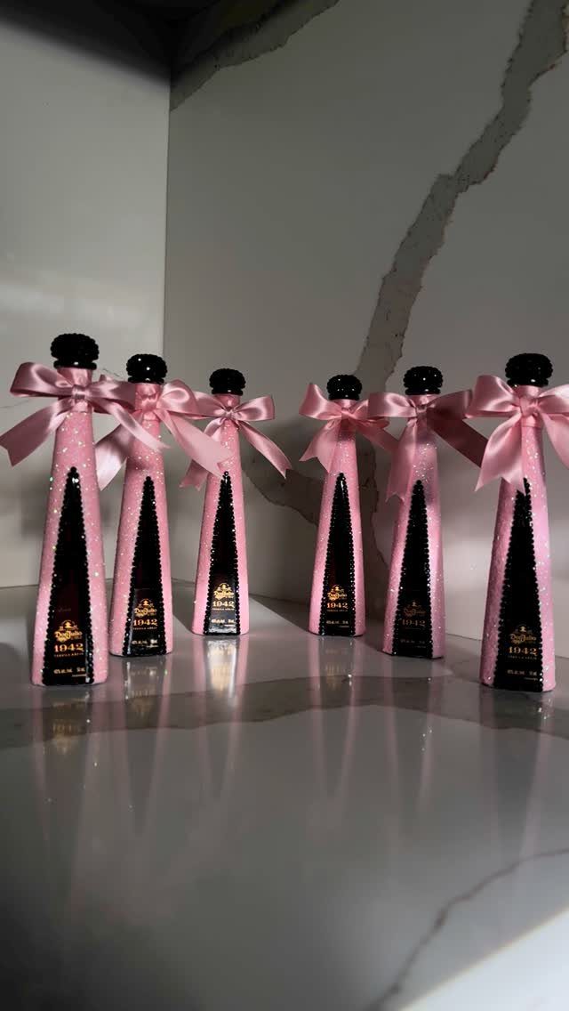 Mini liquor bottles wrapped in pink fabric with satin bows on marble surface