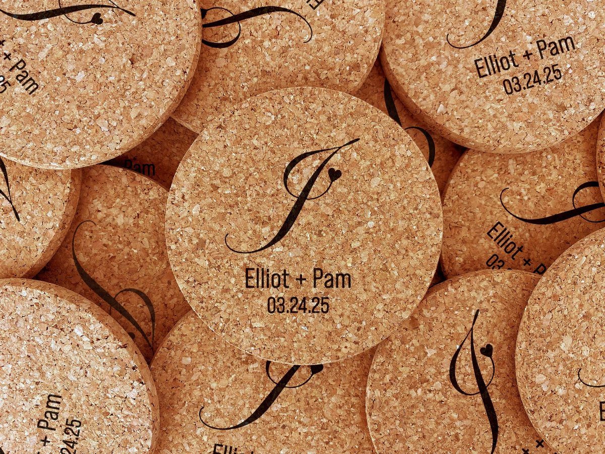 Circular cork coasters with a black monogram, names, and a date printed on them.