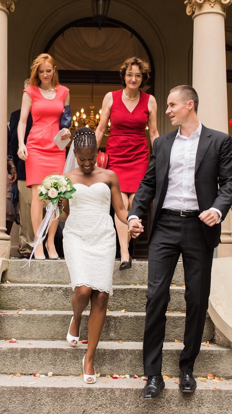 Bride and groom walking down steps followed by bridesmaids in coral and red dresses.