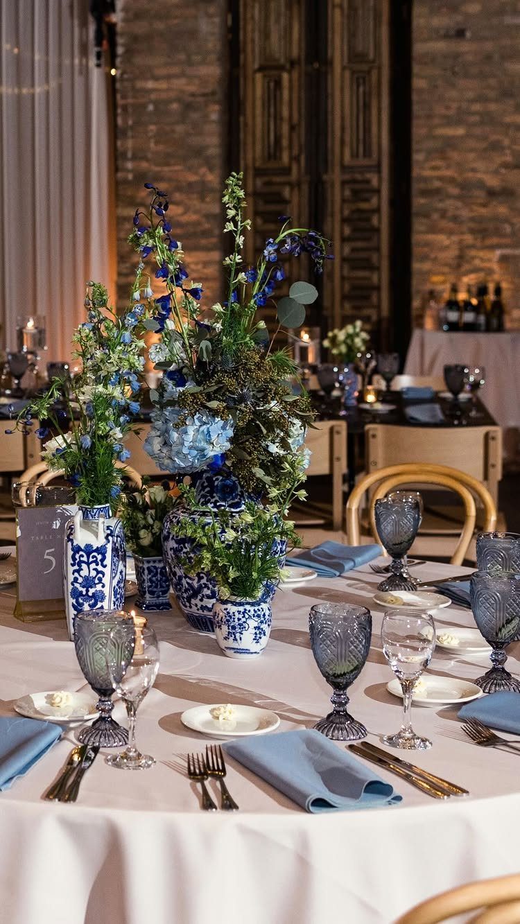 Wedding table setting with white linens, blue napkins, and blue and white floral arrangements.