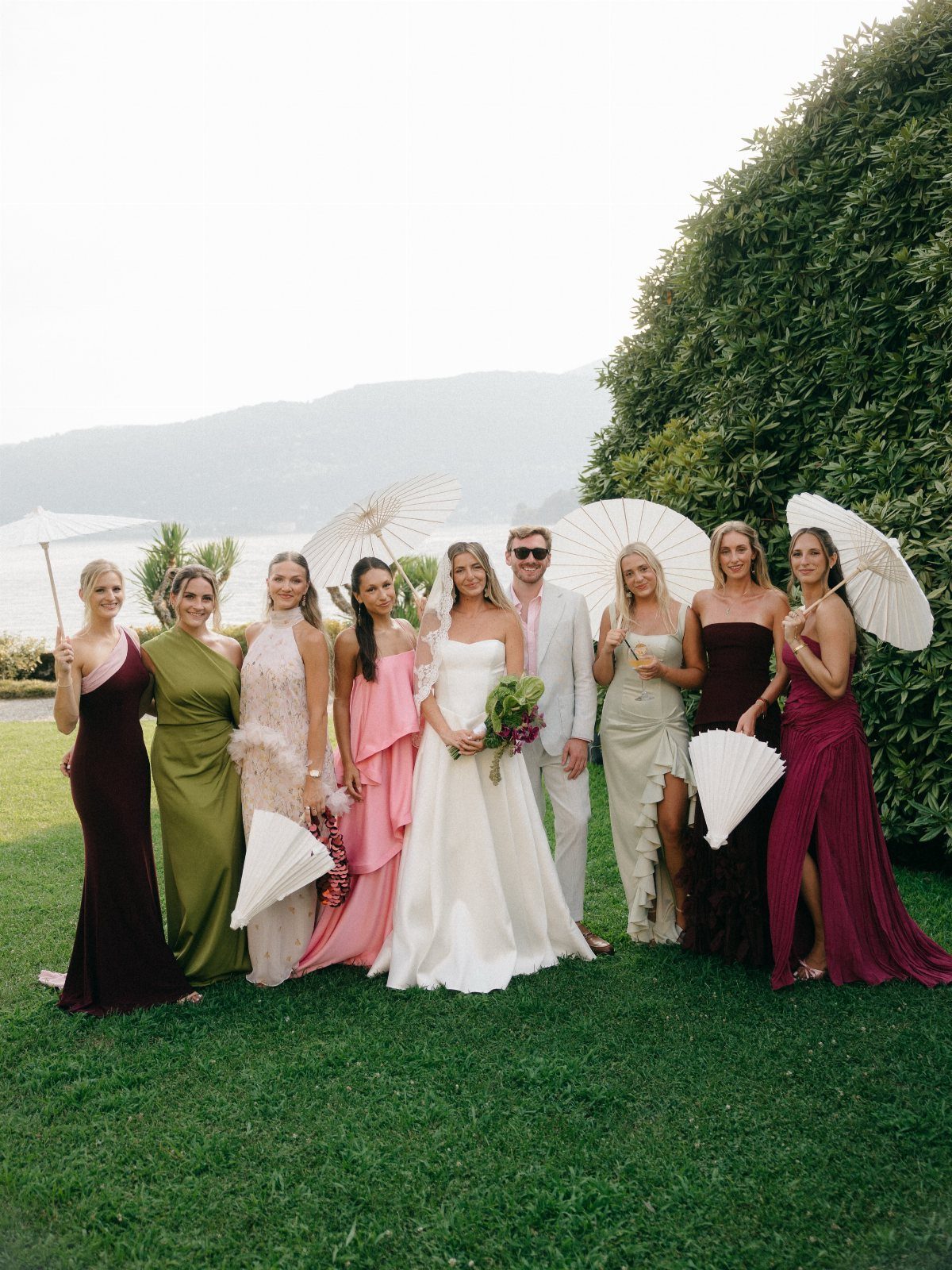 Wedding party posing on a lawn with bridesmaids in various colorful gowns.