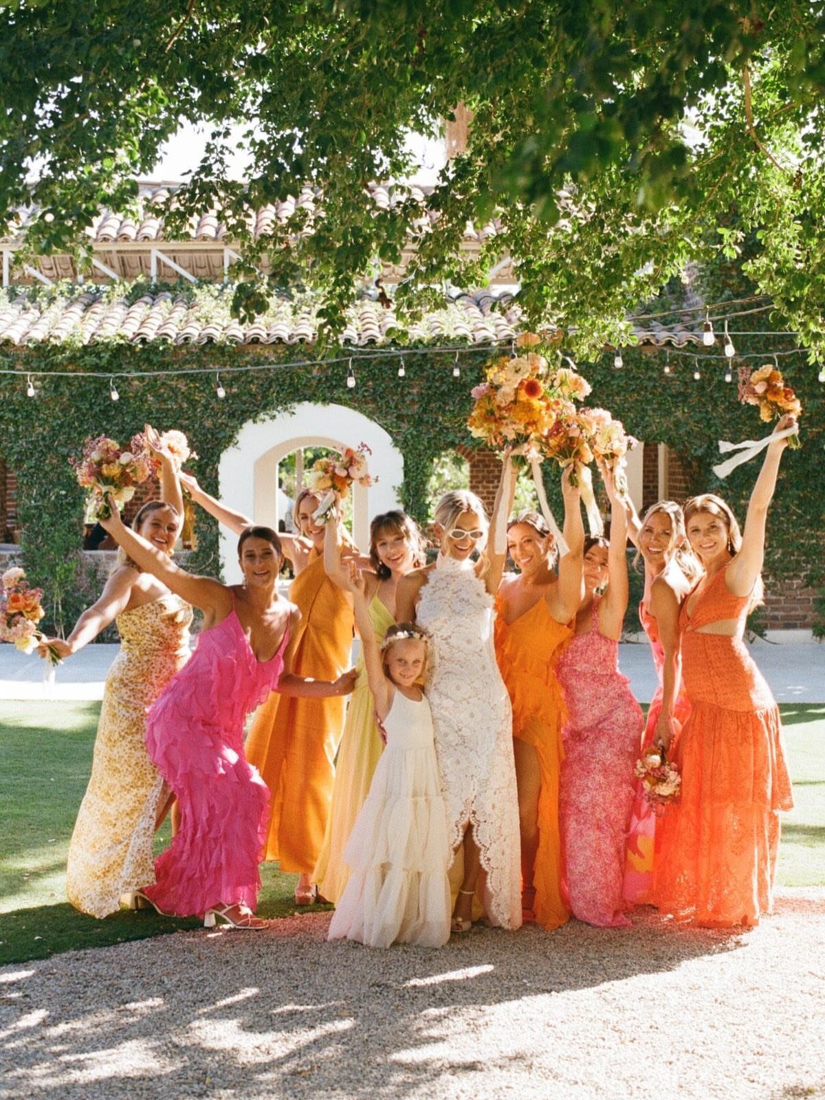 Bride and bridesmaids in yellow, pink, and tropical orange dresses posing in a garden