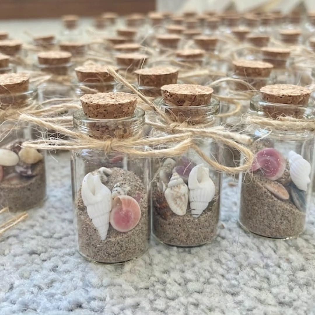 Small glass jars filled with sand and seashells tied with twine bows.