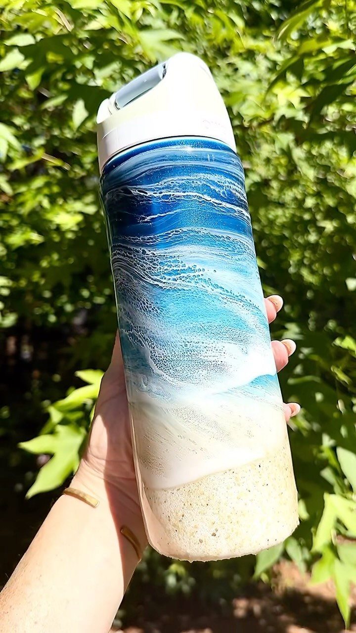 Ocean wave themed tumbler with sandy bottom held against green leaves