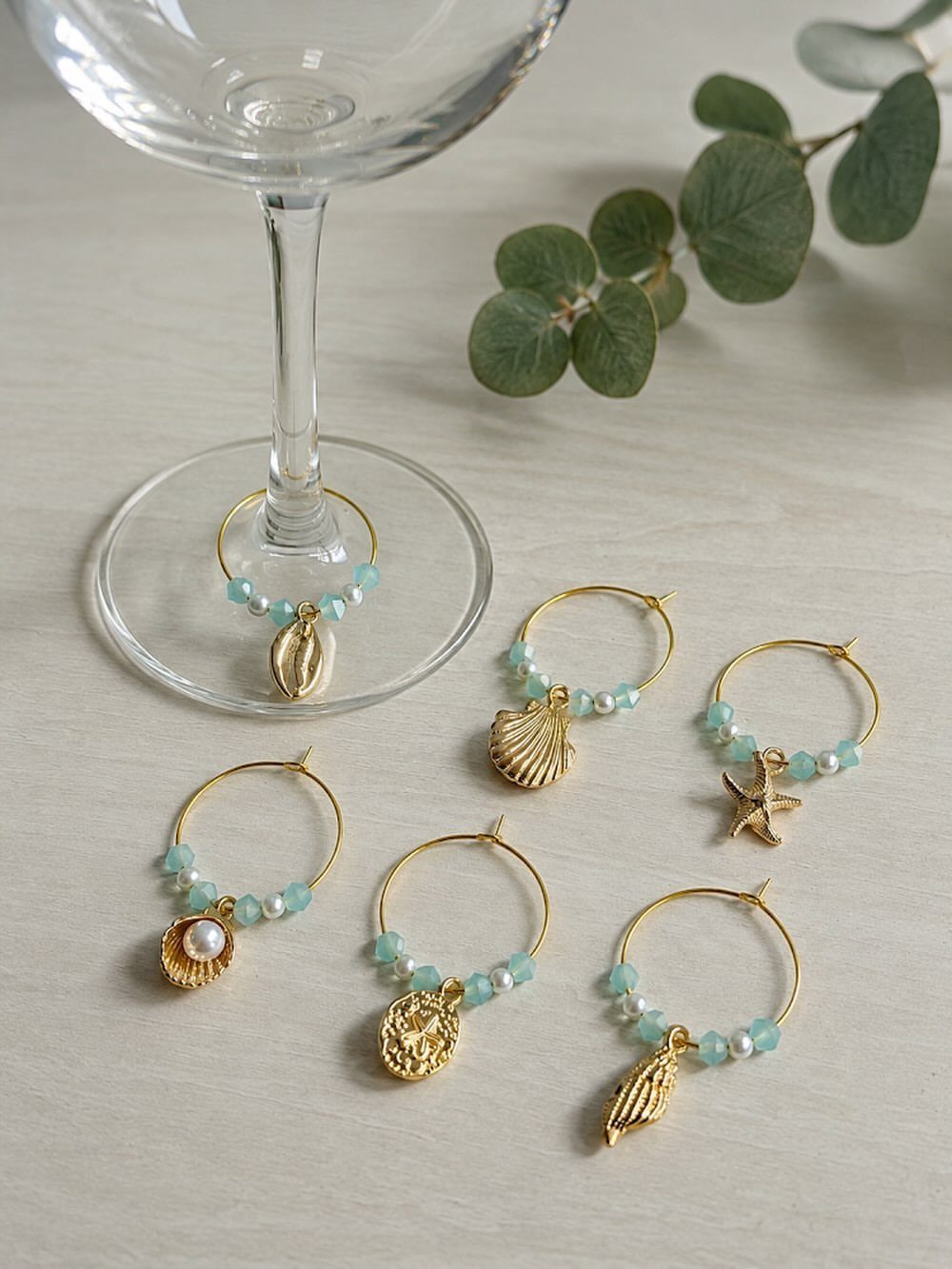 Gold hoop earrings with blue beads and shell charms near a glass goblet.