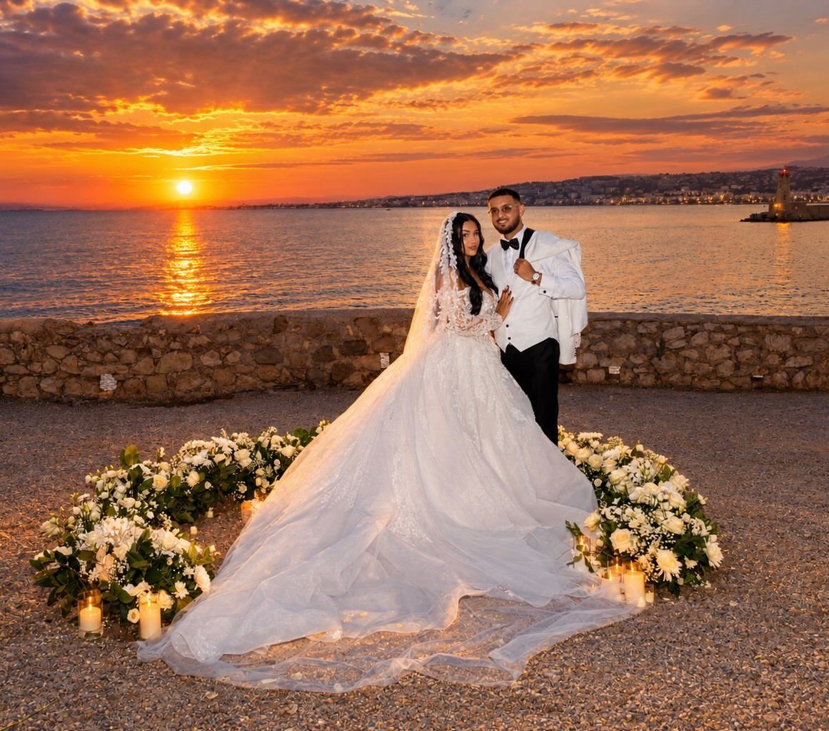 Bride and groom posing by the sea during a vibrant orange coastal sunset.