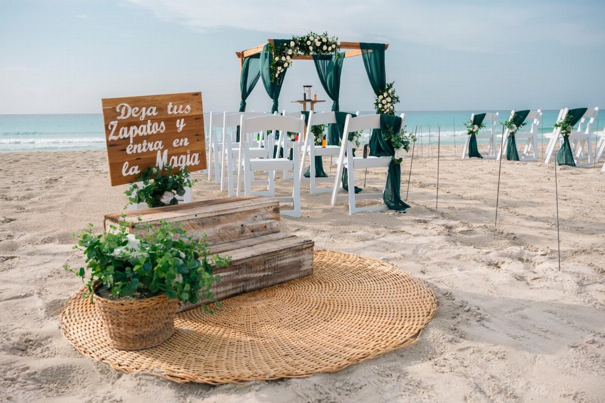 Beach wedding ceremony setup with white chairs and dark green fabric accents on sand