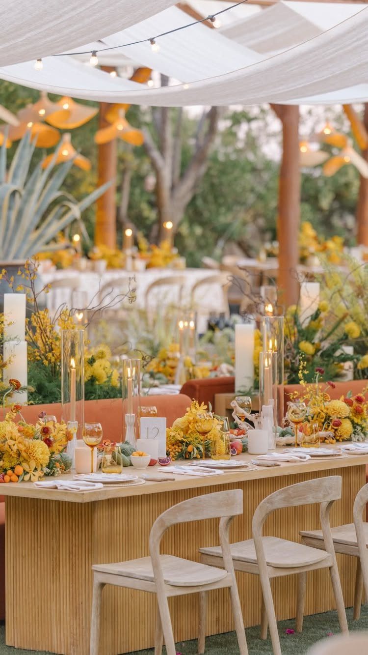 Wedding table with yellow flowers and light wood chairs under a white canopy.