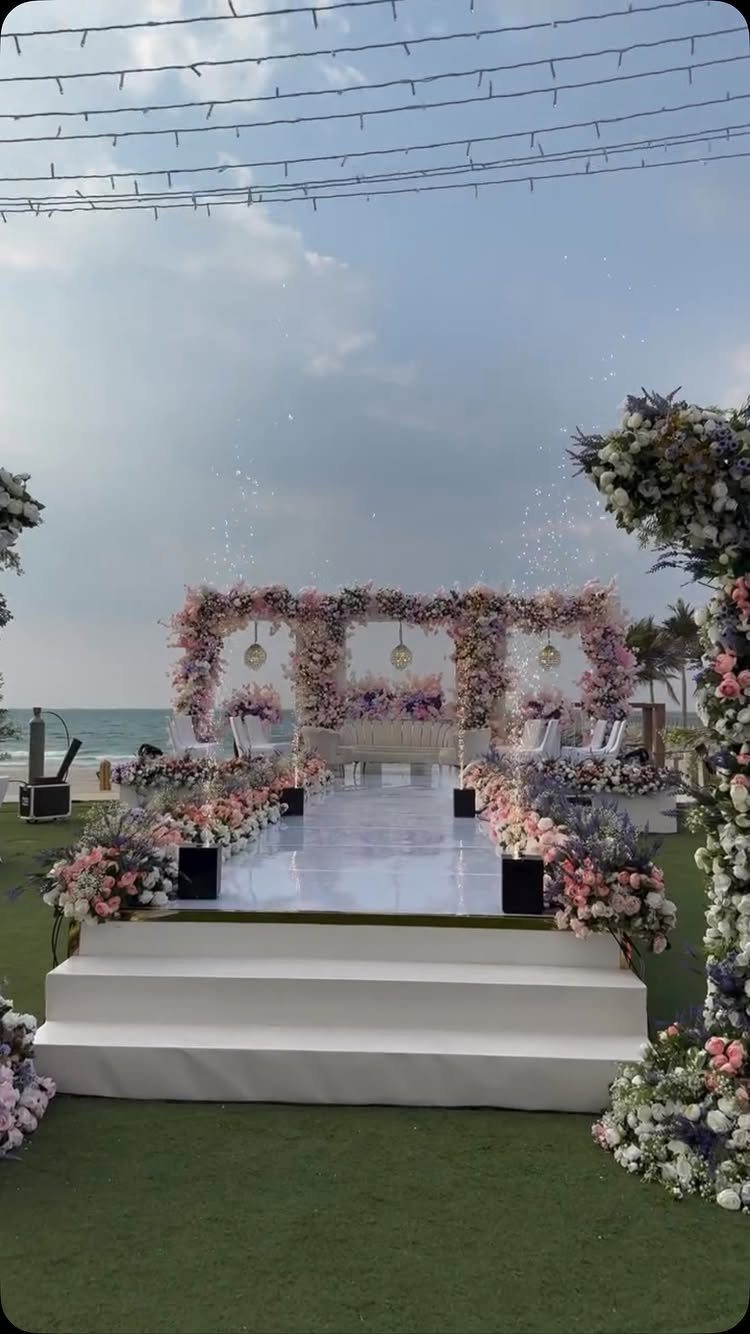 White wedding aisle and floral arch with pink and purple flowers on a beach