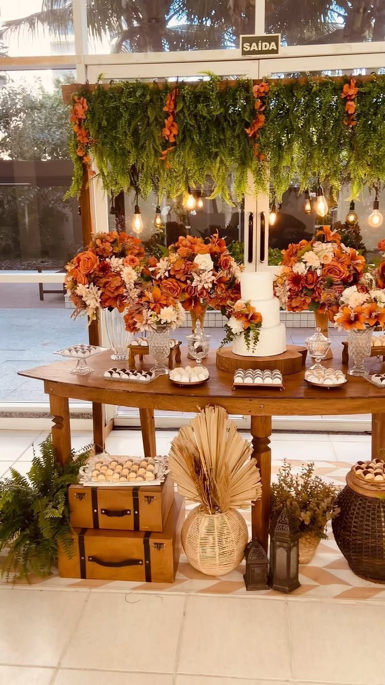 Wedding dessert table with orange flowers, white cake, and hanging greenery decorations.