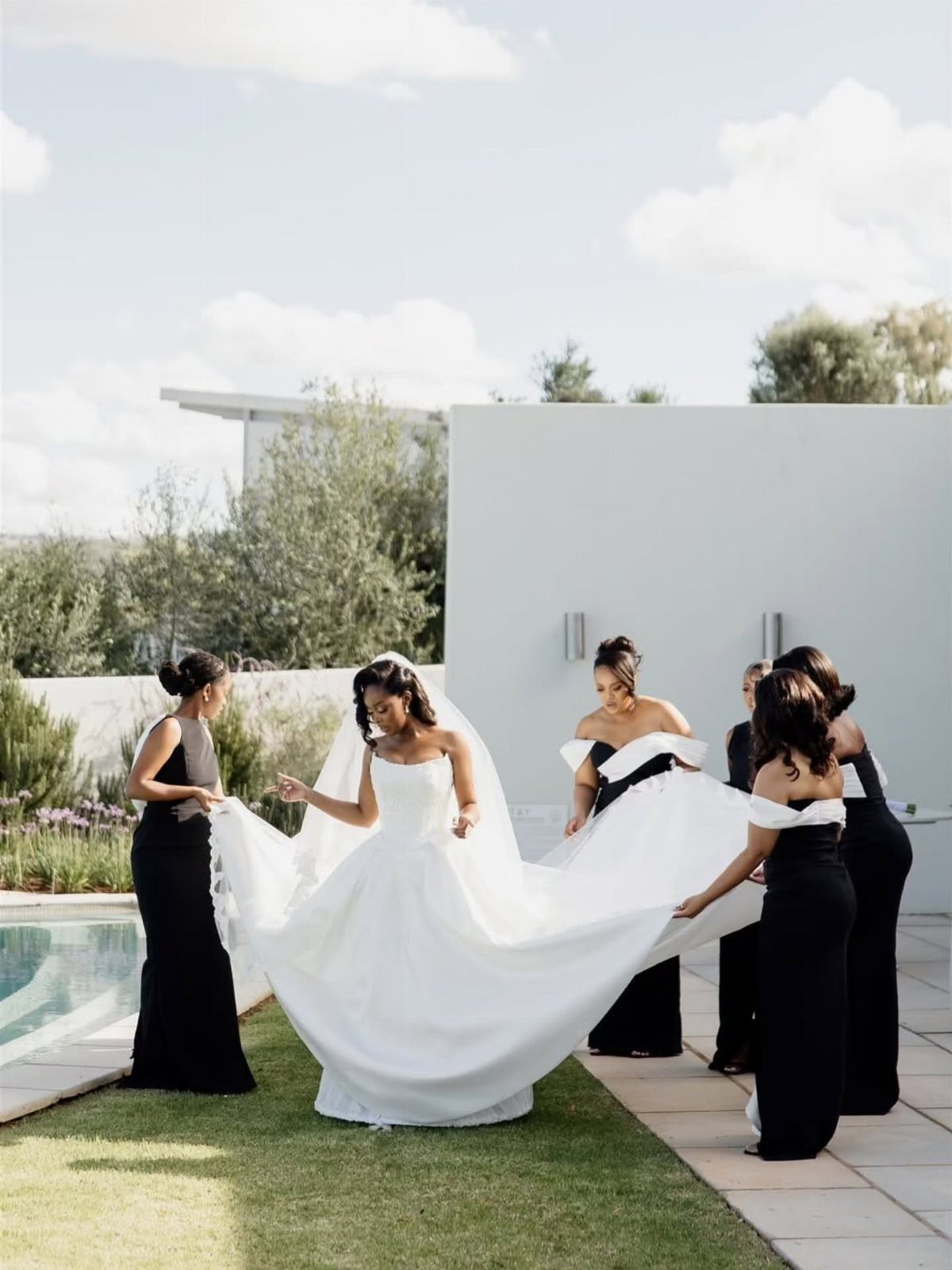 Bride in white gown with bridesmaids in black dresses on a sunny patio.