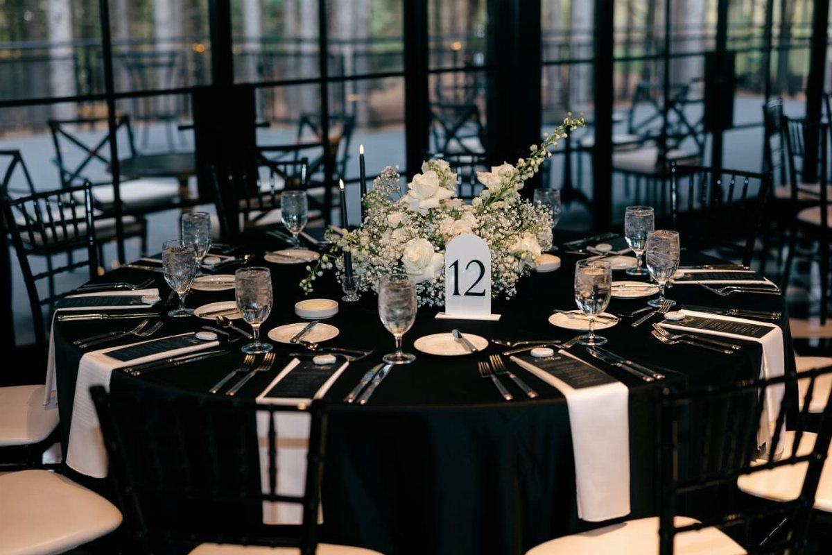 Round wedding table with black tablecloth, white napkins, and white floral centerpiece.