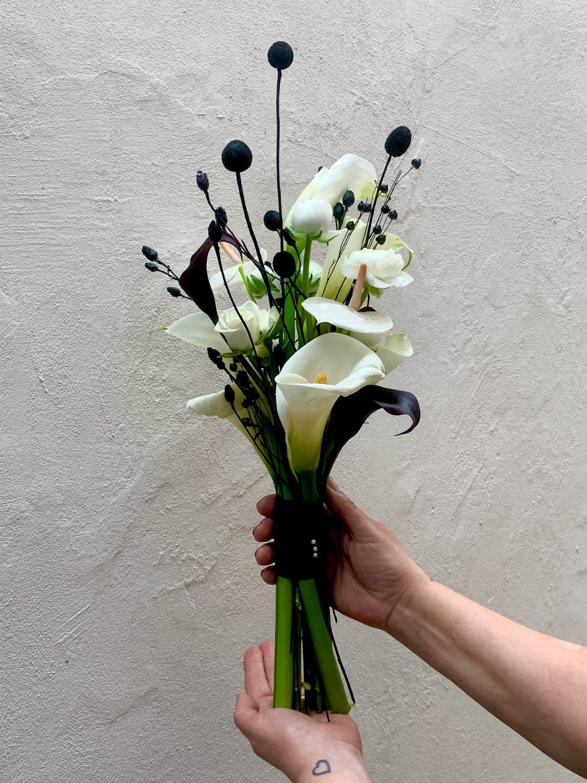 Bridal bouquet with white calla lilies and black berries held against a grey wall