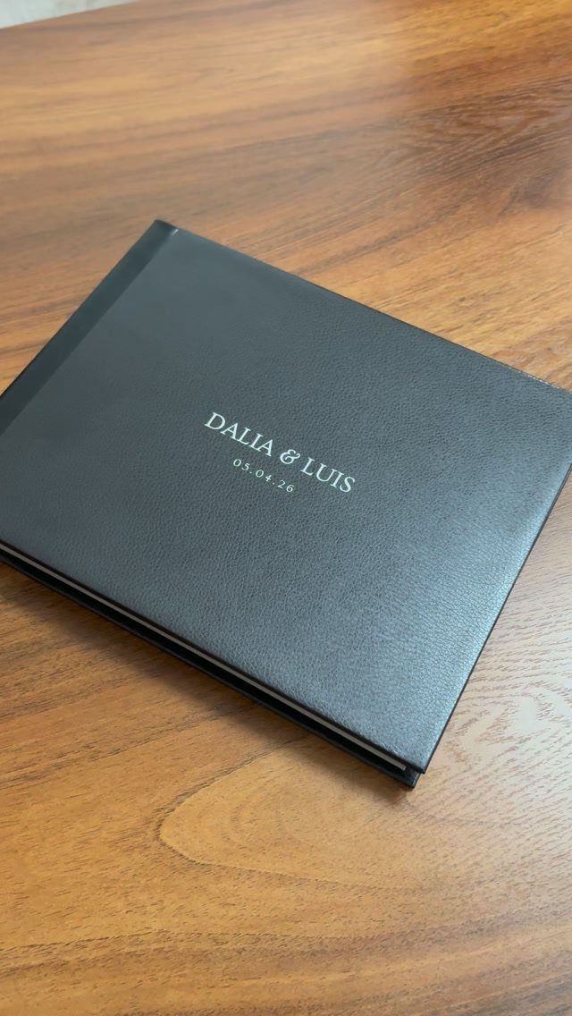 Black hardcover guest book with silver names and date on a wooden table