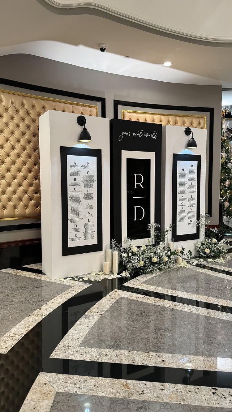 Black and white wedding seating charts on white panels with floral accents.