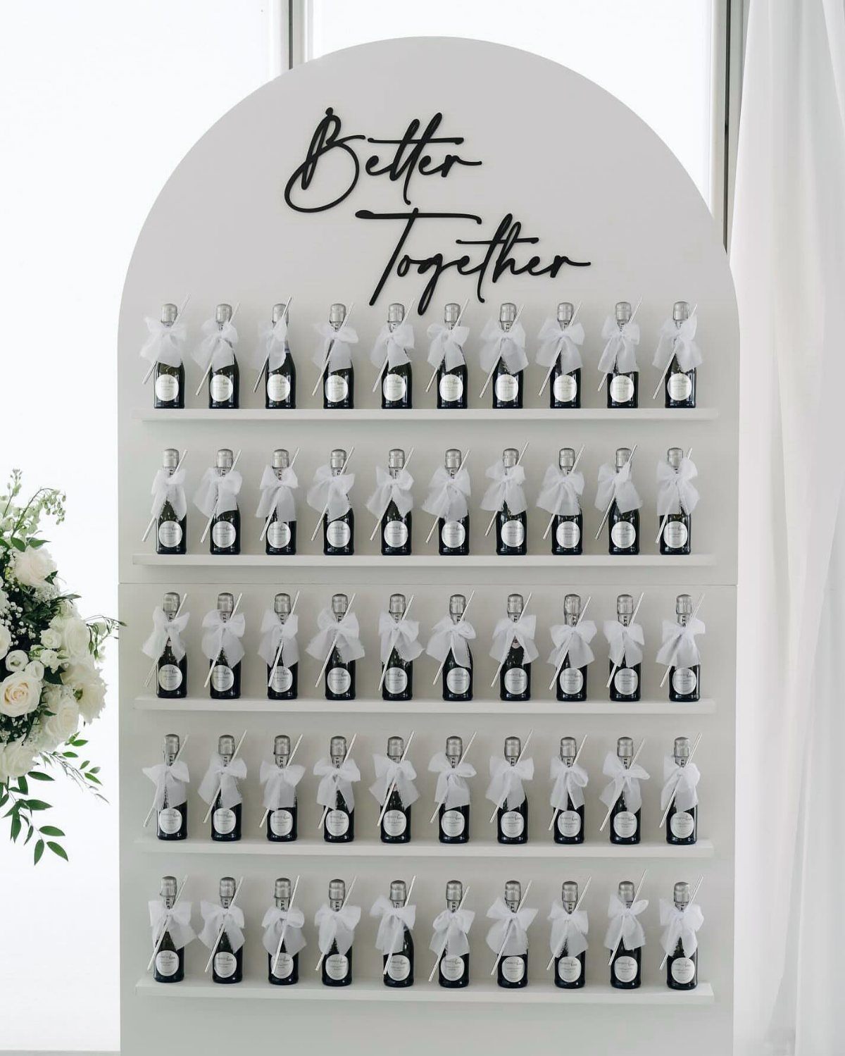 Small dark bottles with white ribbons on a white arched display wall