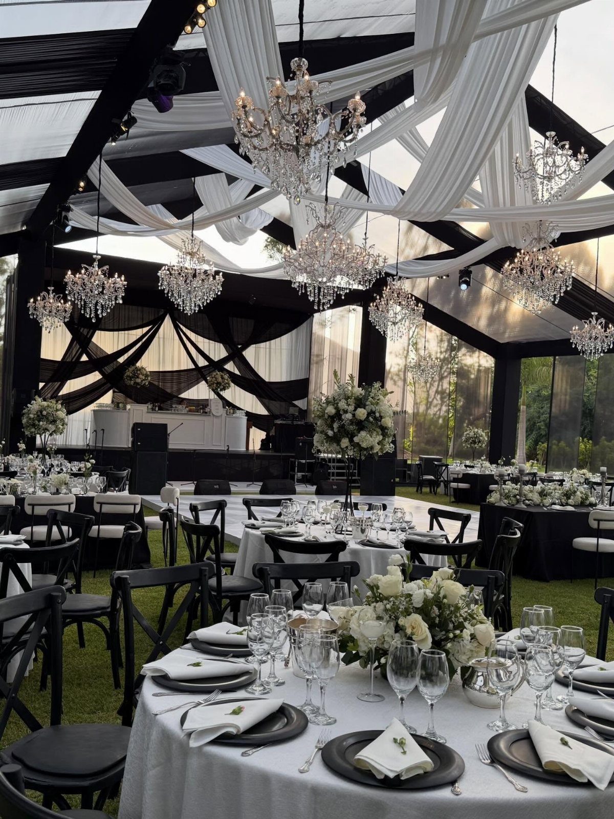 Black and white wedding reception setup with chandeliers, draped fabric, and elegant table settings.