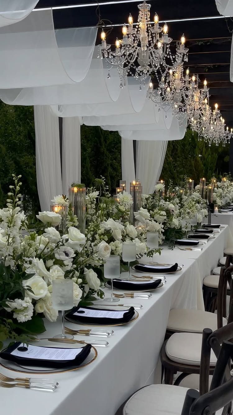 Wedding banquet table with white flowers, black napkins, and crystal chandeliers overhead.