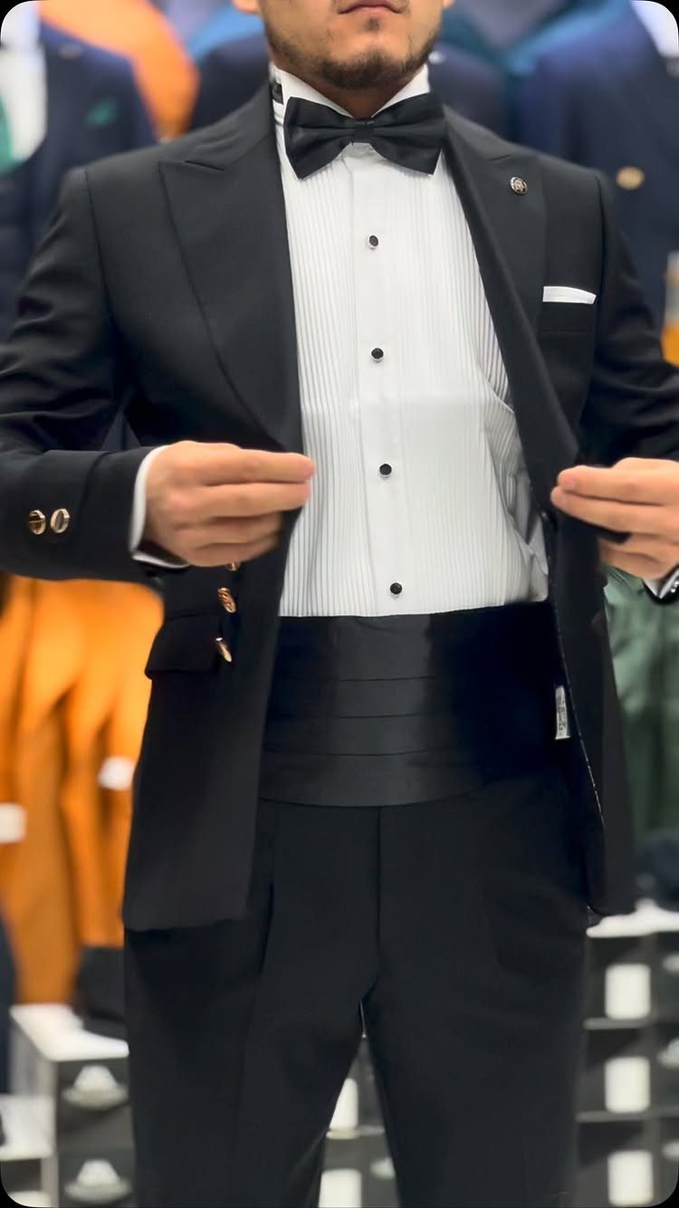 Man wearing a formal black tuxedo with a bow tie and black cummerbund.