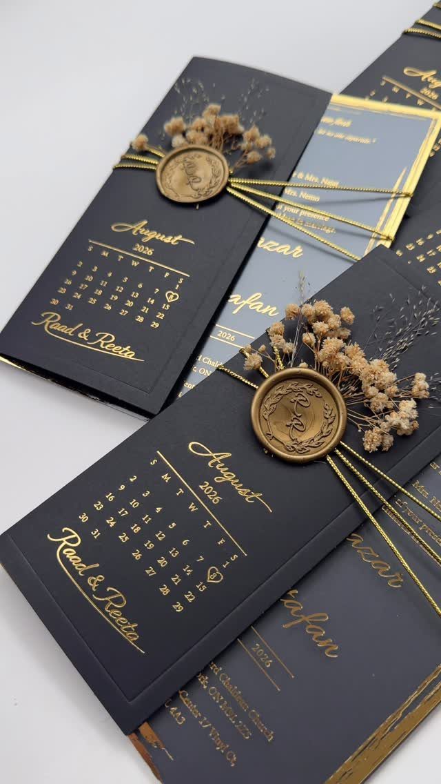 Black wedding invitations with gold foil lettering, wax seals, and dried flowers.