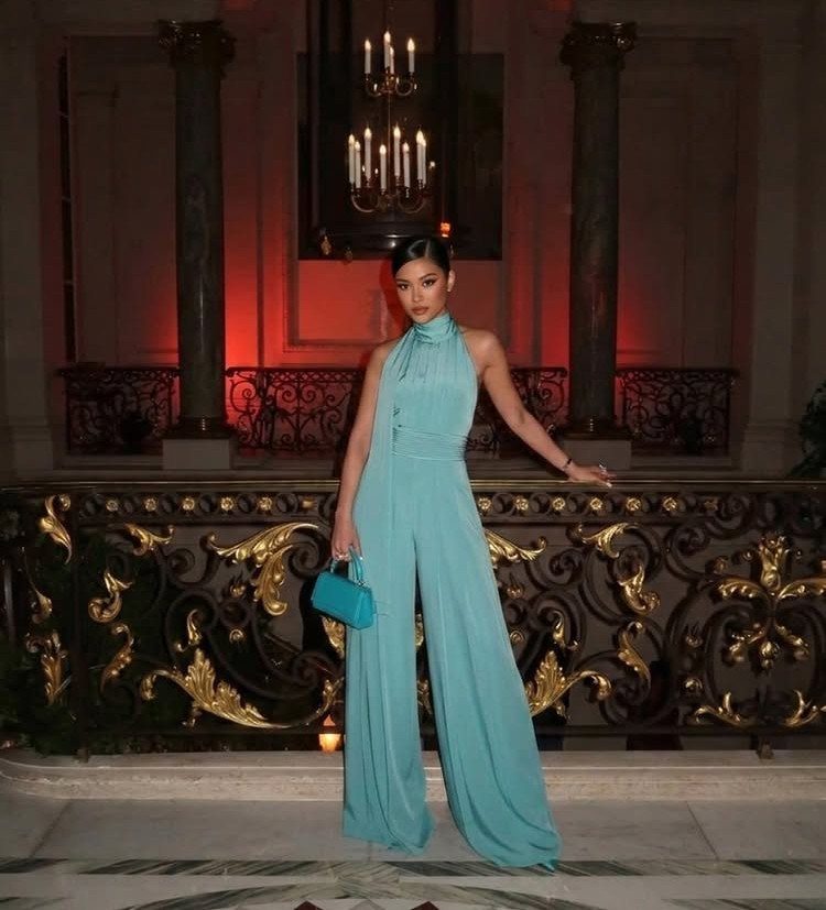 Woman in a light blue wide-leg formal jumpsuit posing in a grand hall.