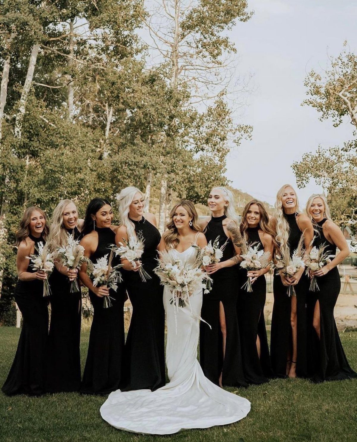 Bride in white gown surrounded by bridesmaids wearing mismatched black floor-length dresses.