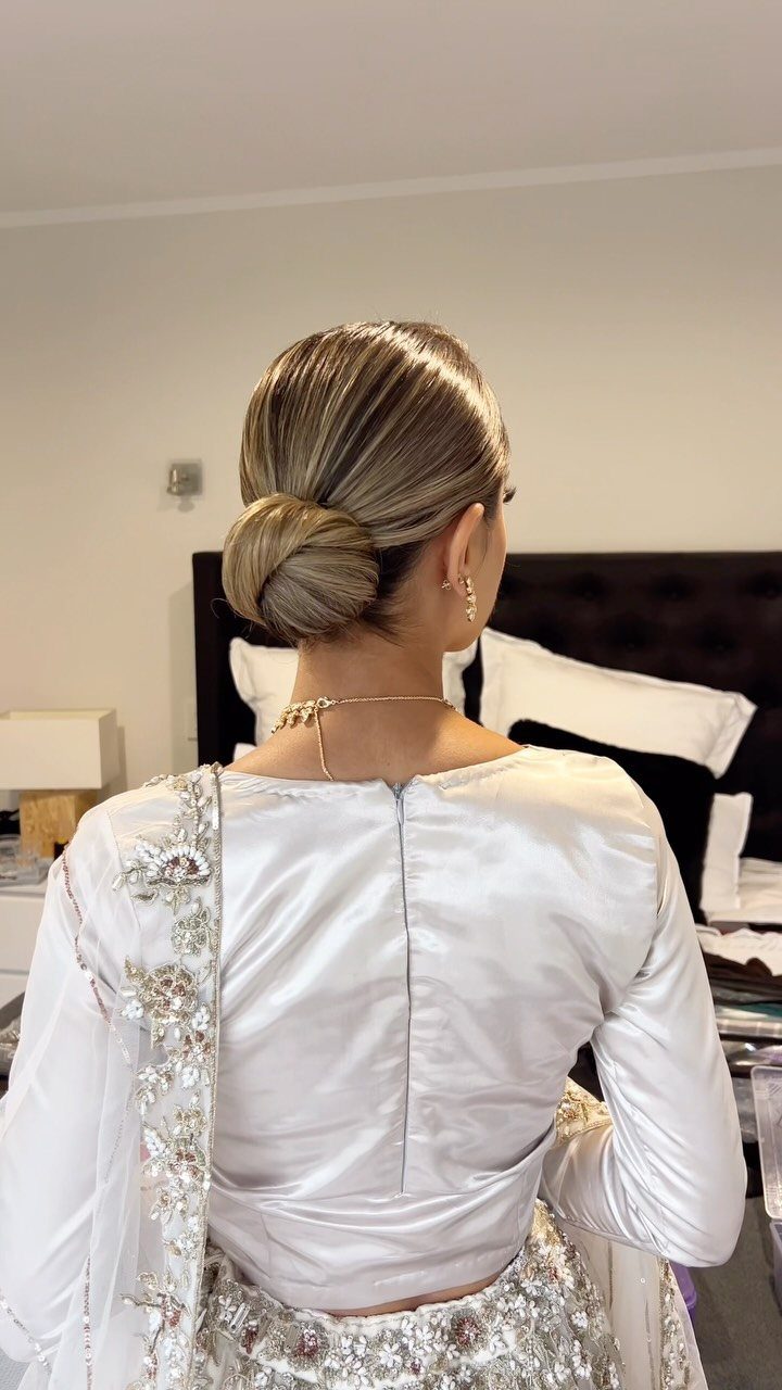 Woman with a sleek low bun hairstyle wearing a white satin embroidered outfit.