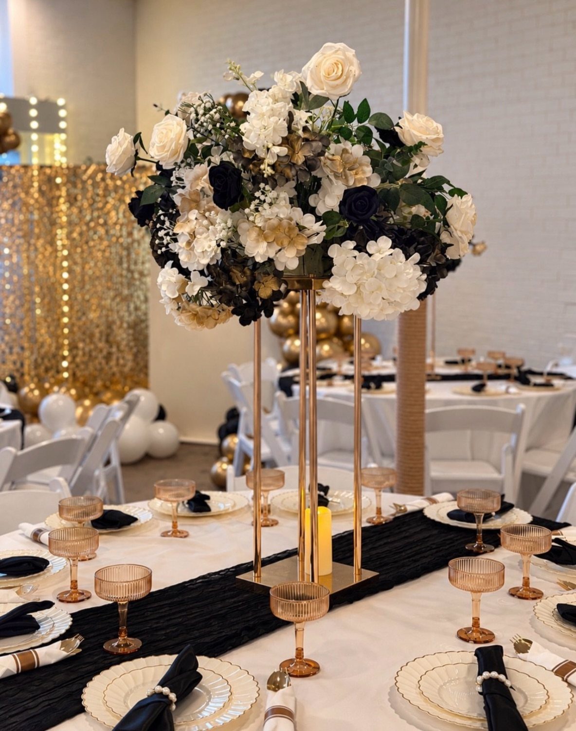Tall floral centerpiece with white and black roses on a gold stand.