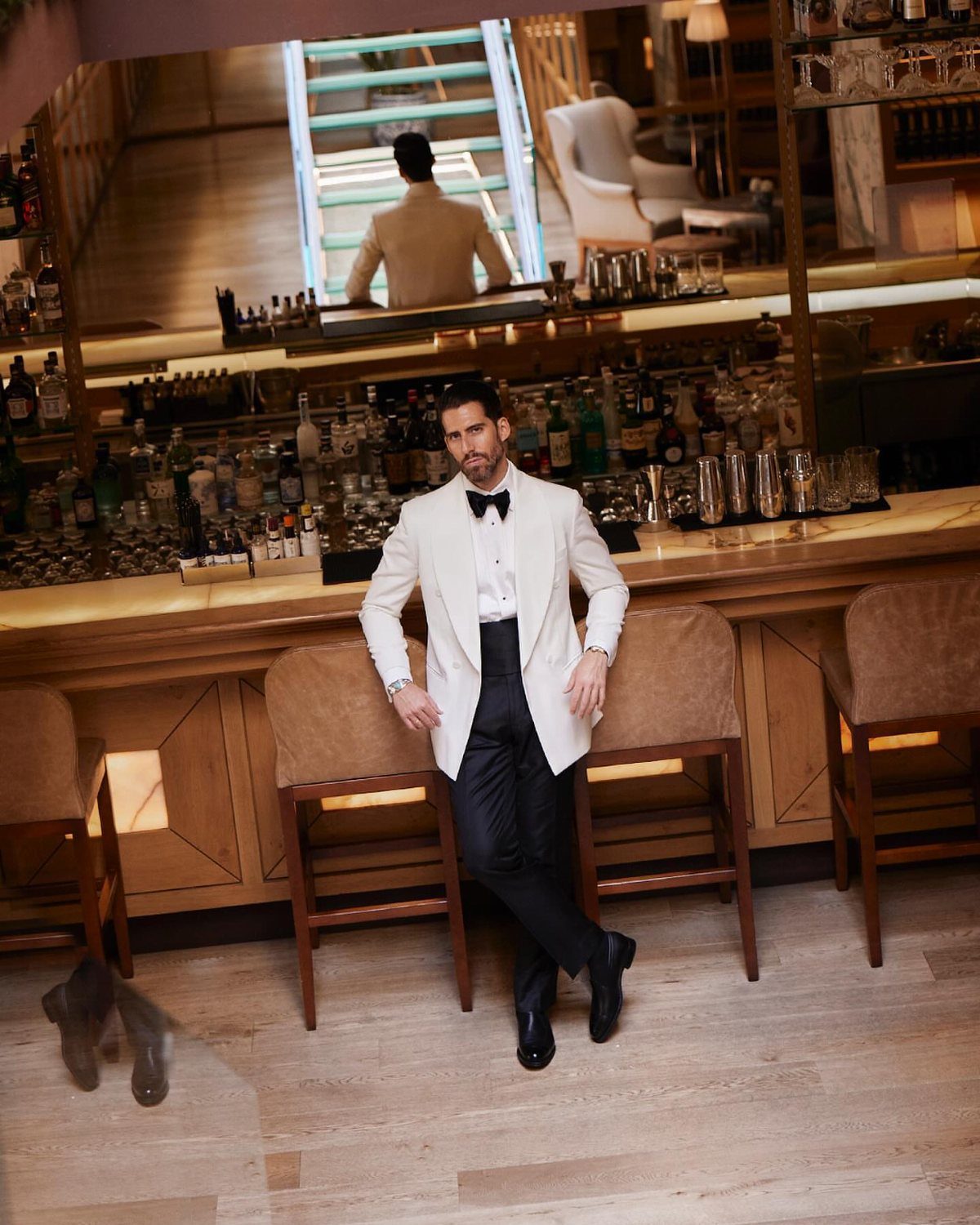 Man in white tuxedo jacket and black bow tie leaning against a bar.