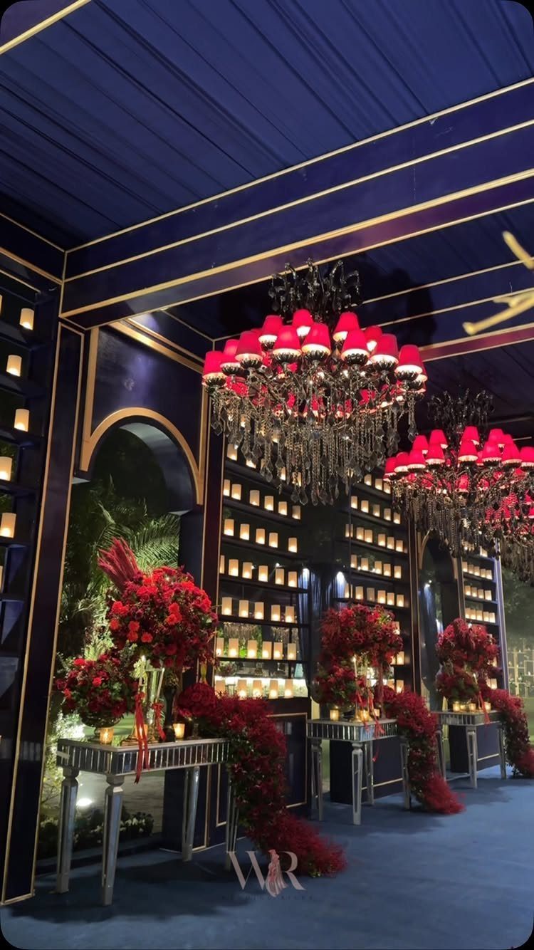Deep blue event space with red floral arrangements and red shaded chandeliers.