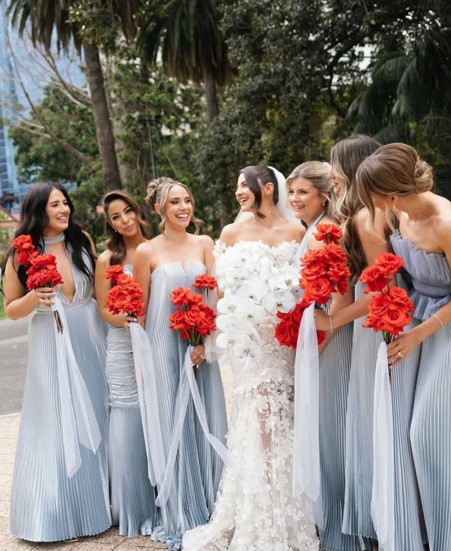 Bride in white gown with bridesmaids in light blue dresses holding red roses.