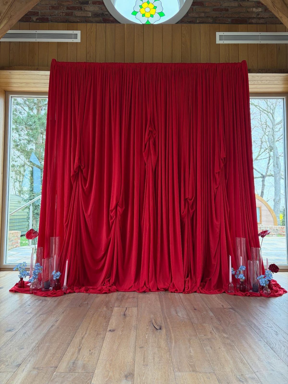 Red velvet curtain backdrop with red and blue floral arrangements on wooden flooring