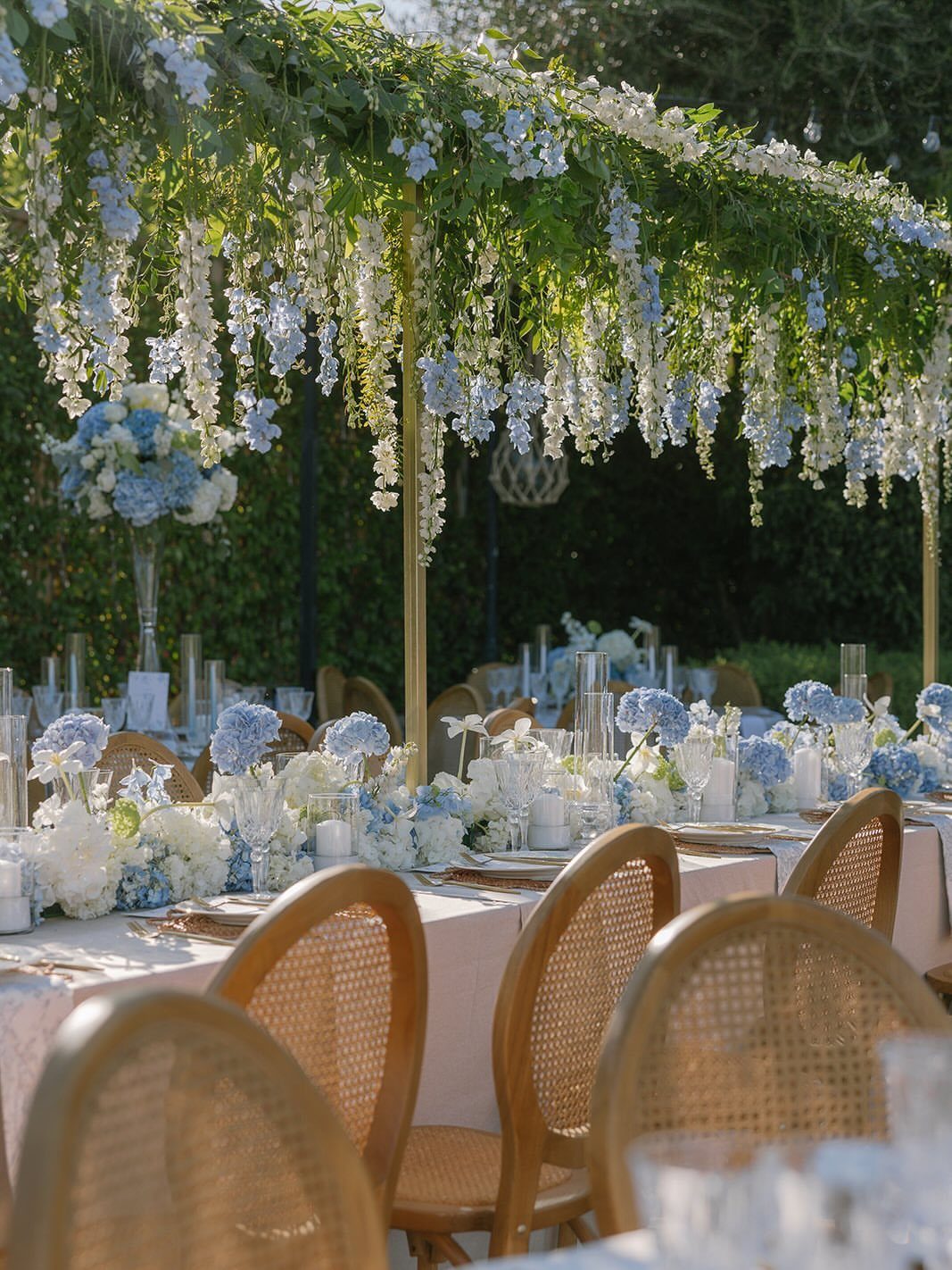 Wedding table with baby blue and white flowers under a floral wisteria canopy