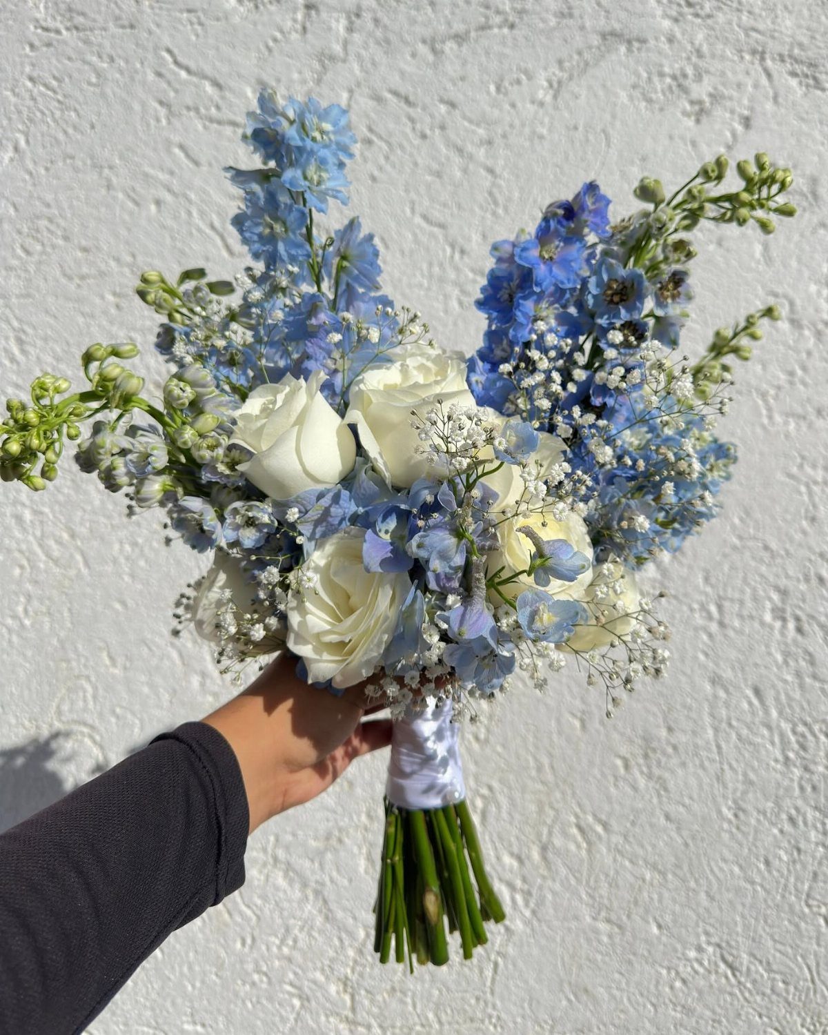 Wedding bouquet with light blue delphiniums and white roses against a white wall