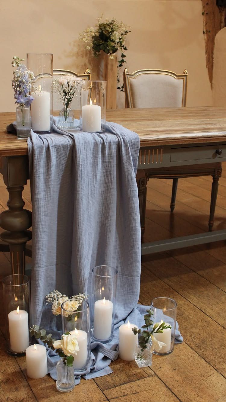 Dusty blue fabric runner on a wooden table with white candles and flowers.