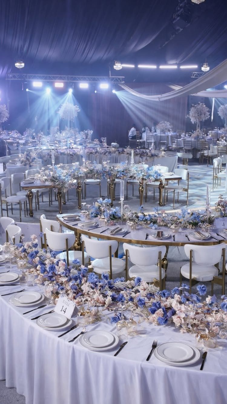Wedding reception tables with white linens and extensive light blue floral centerpieces.