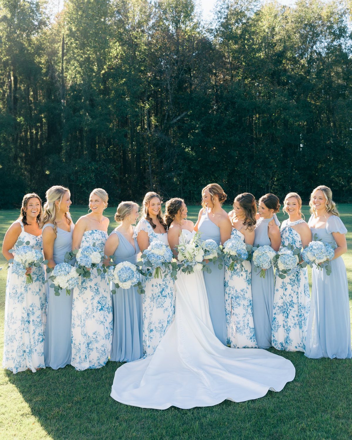 Bride and bridesmaids in light blue dresses posing outdoors with blue floral bouquets.