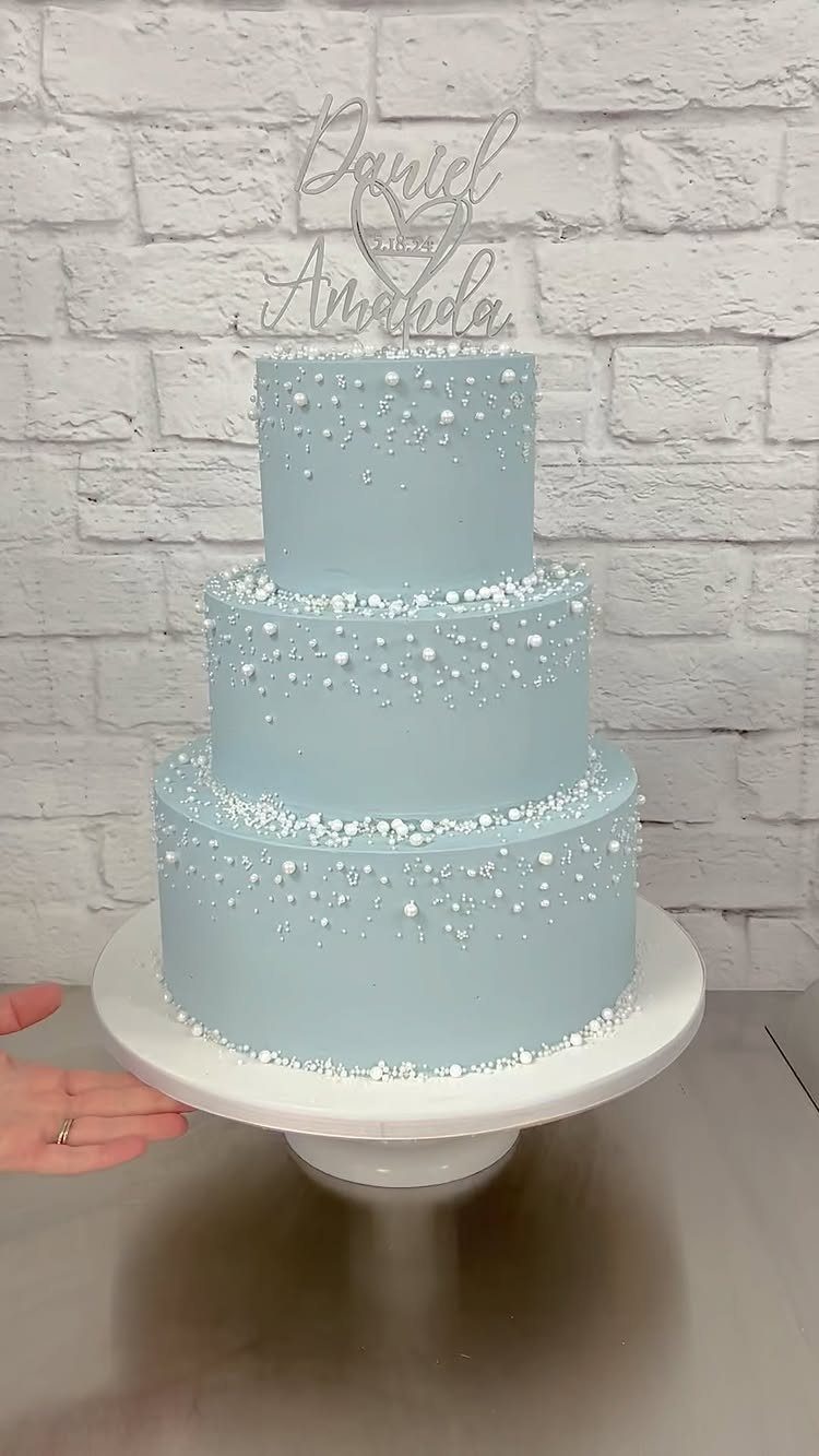 Three-tiered light blue wedding cake with white pearl decorations and a silver topper.