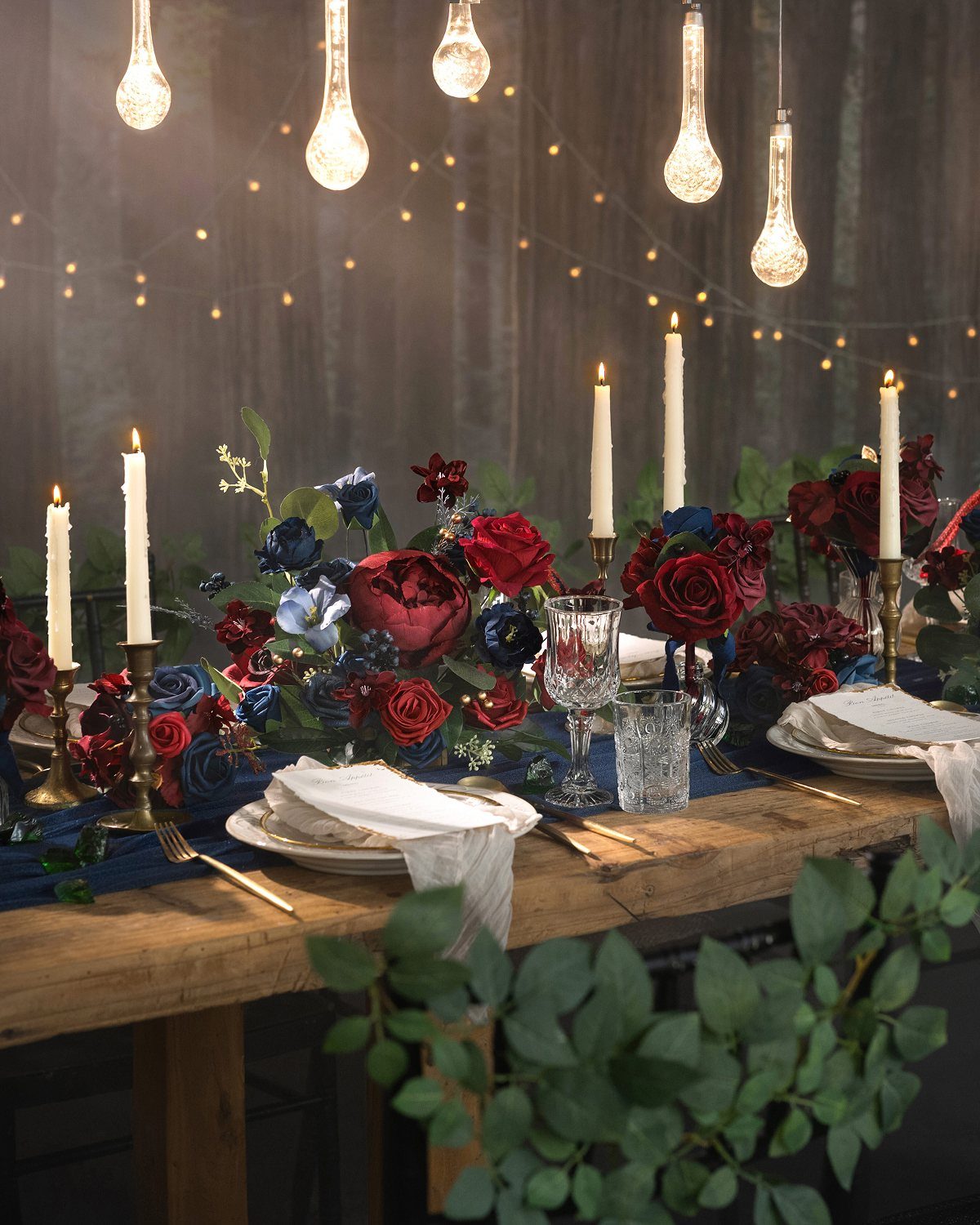 Wooden table with midnight blue runner, red roses, and hanging light bulbs.