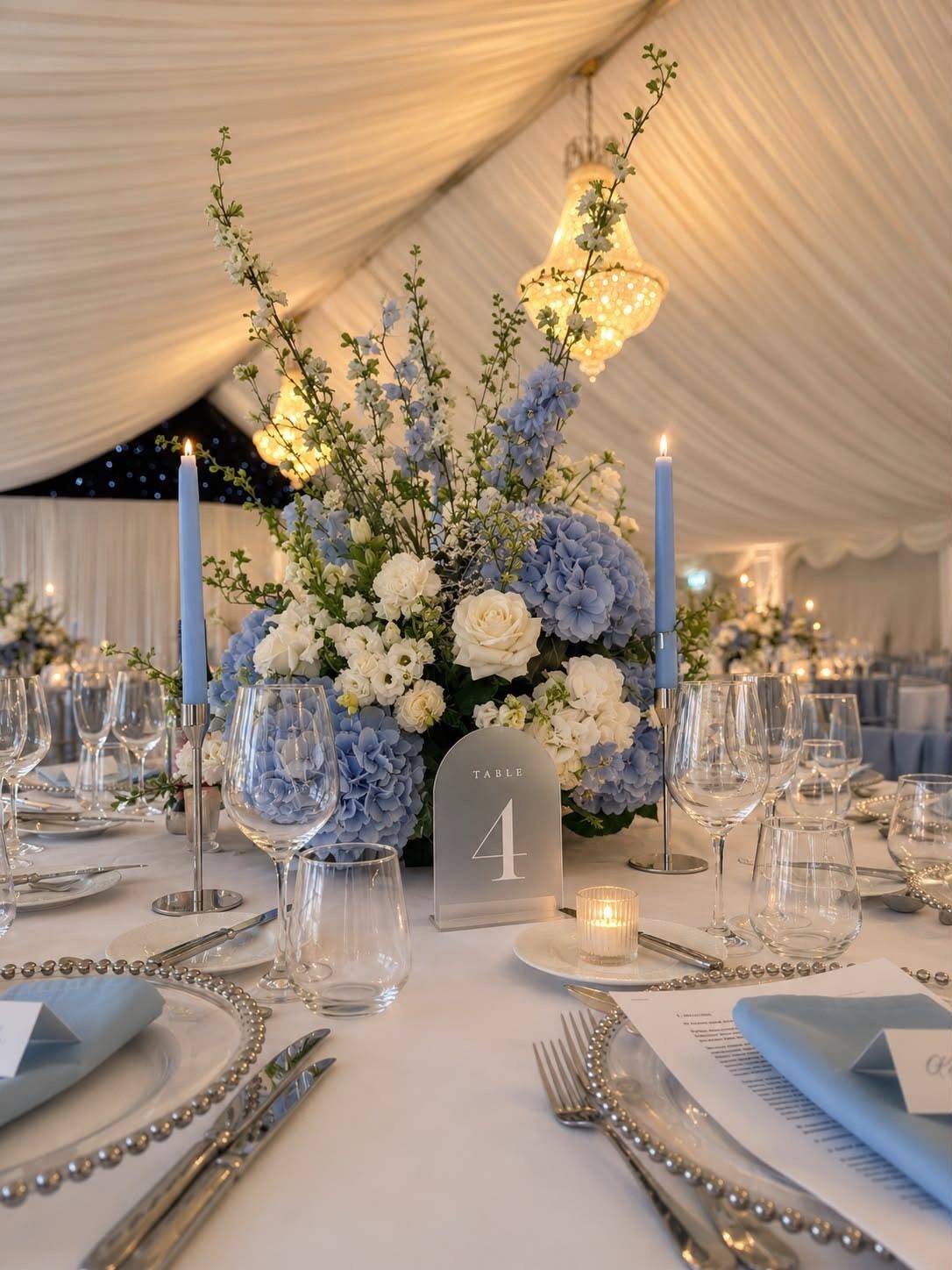 Wedding table setting with powder blue flowers, blue candles, and white linens.
