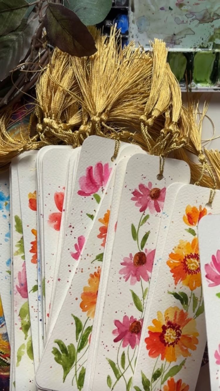 Watercolor floral bookmarks with gold tassels arranged in a stack on a table
