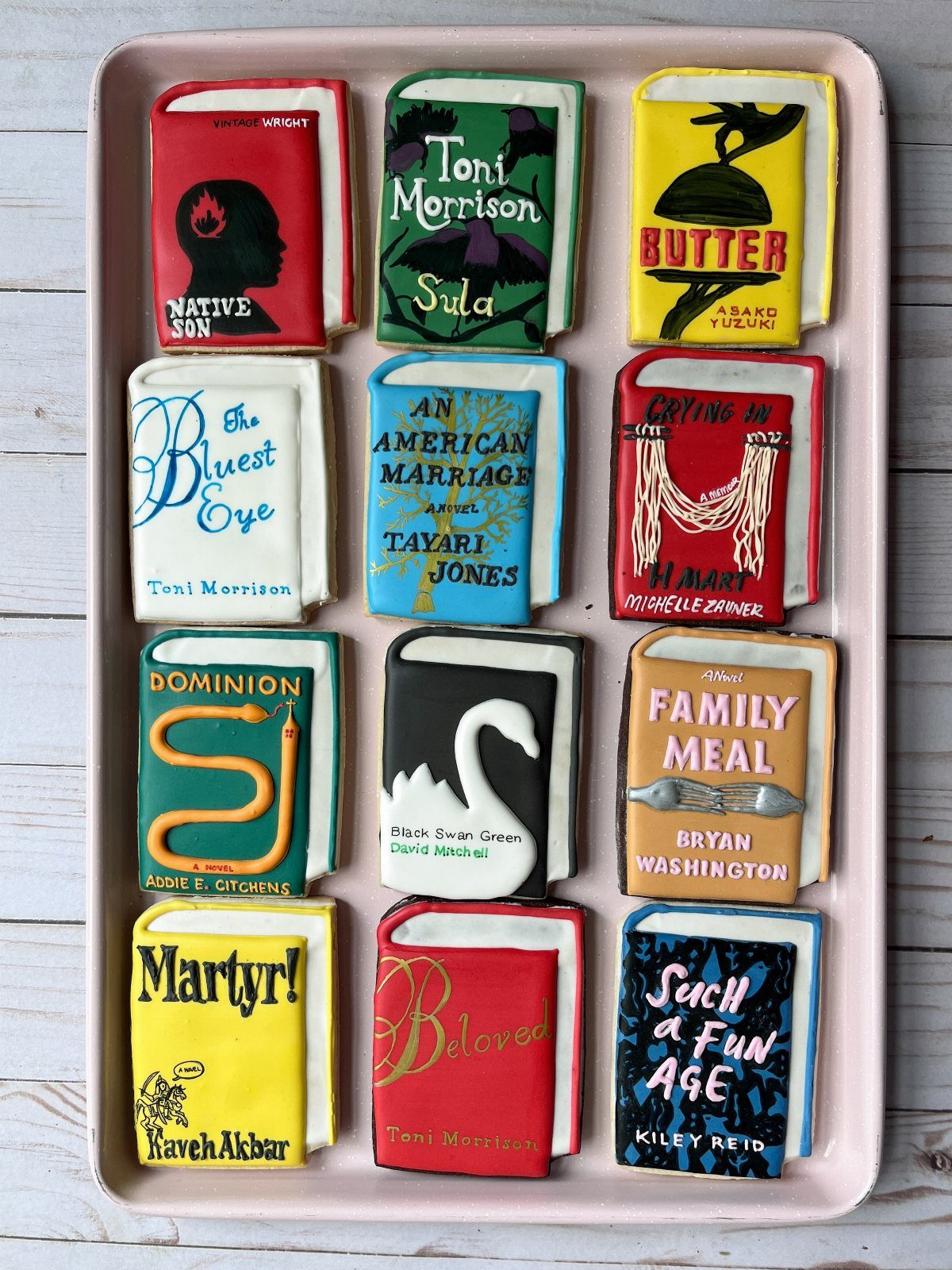Book shaped cookies with detailed icing covers arranged in a pink tray.