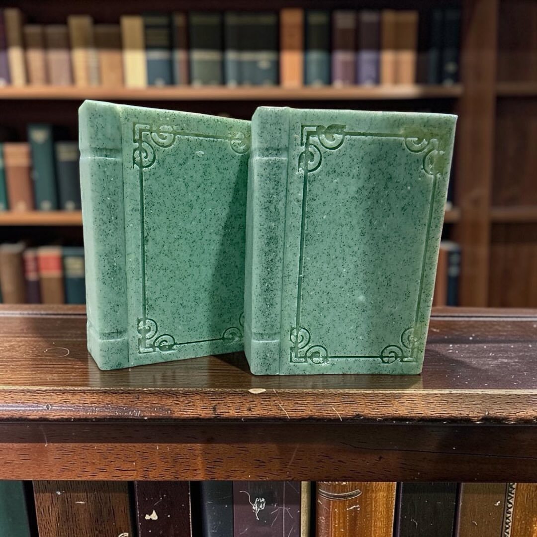 Two green book-shaped soaps with embossed details on a wooden library shelf.