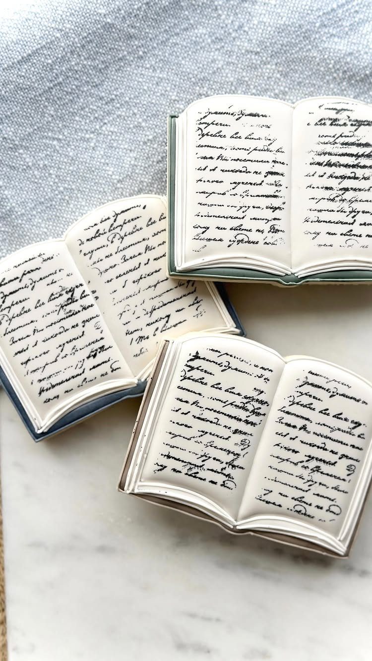 Three small ceramic open books with handwritten script on a marble surface.