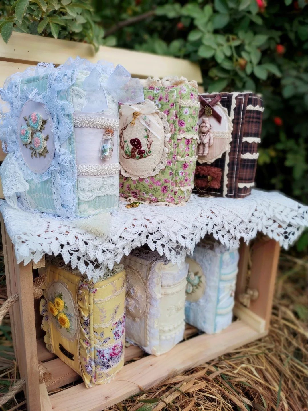 Vintage fabric notebooks with lace and floral details displayed on a wooden crate.