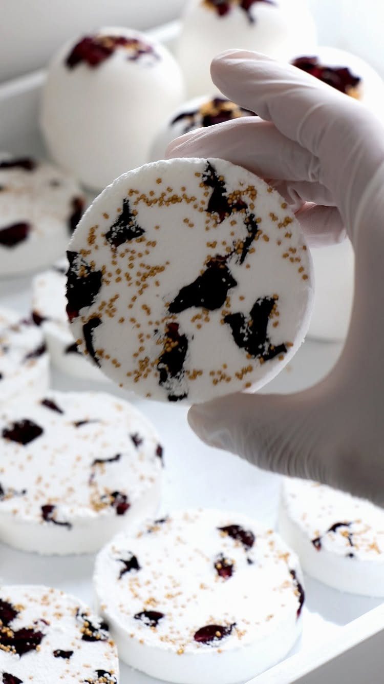 White bath bombs with red petals and gold glitter held by gloved hand.