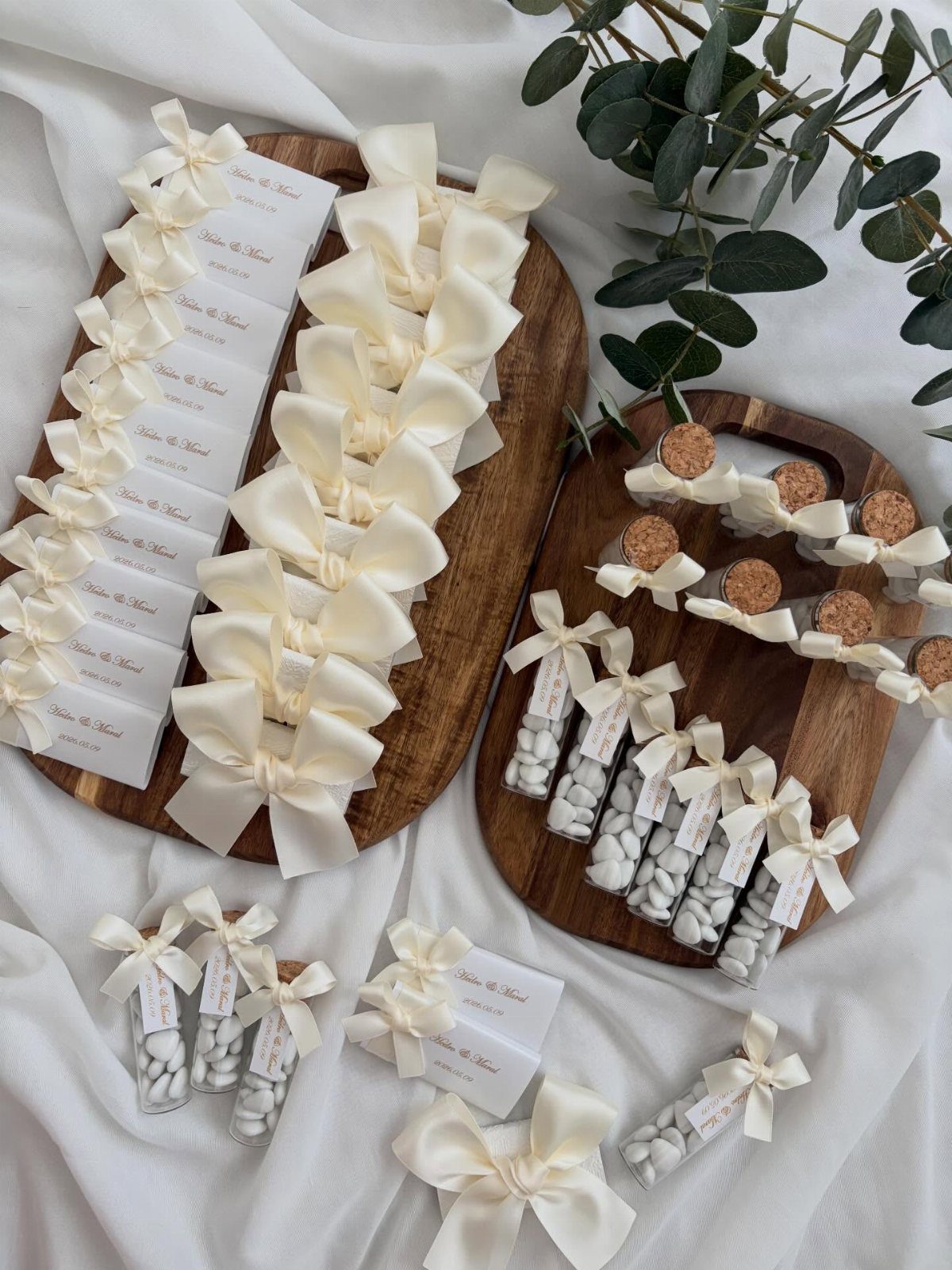 White candy vials and gift boxes with cream bows on wooden boards.
